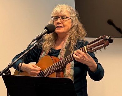 Woman playing guitar at open mic representing heart-centered creative practice and embodied presence